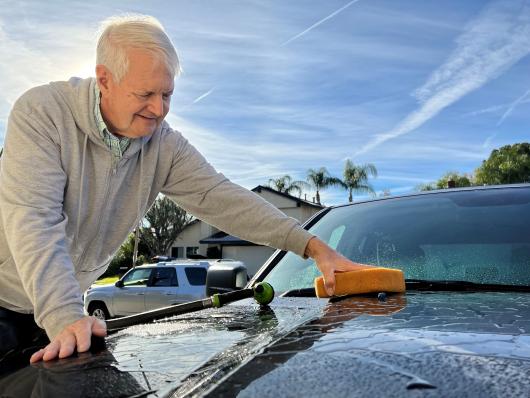 Homeowner washing his car using a hose with a shut-off nozzle.